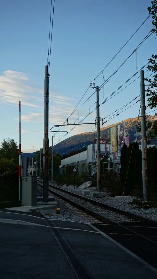 Bahngleise mit Signal und Berglandschaft im Hintergrund unter blauem Himmel.