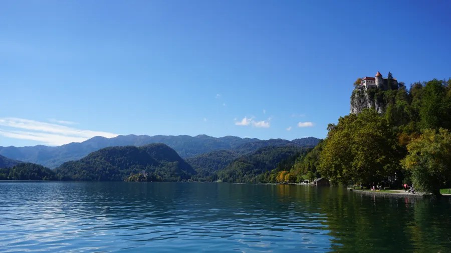 Ein Blick auf den bleder See mit sanften Bergen im Hintergrund und einer Burg auf einem Felsen.
