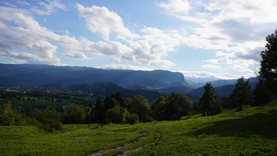 Panoramablick auf grüne Wiesen und Berge unter einem blauen Himmel mit Wolken.