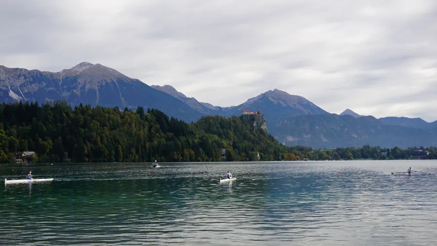 Ruderer auf einem See mit Bergen im Hintergrund und bewölktem Himmel.