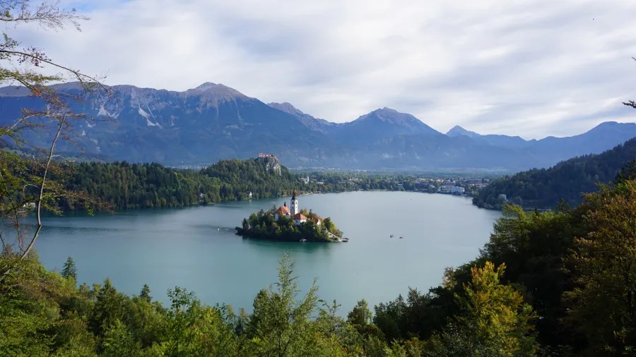 Panoramablick auf den Bleder See mit der kleinen Insel und der Kirche im Vordergrund, umgeben von Bergen und Wäldern.