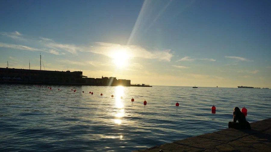 Sonnenuntergang über dem Wasser mit einer Person, die am Ufer sitzt und pinkfarbene Bojen im Wasser schwimmen sieht.