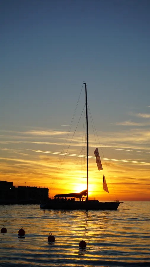 Ein Segelboot fährt vor einem Sonnenuntergang auf ruhiger See.