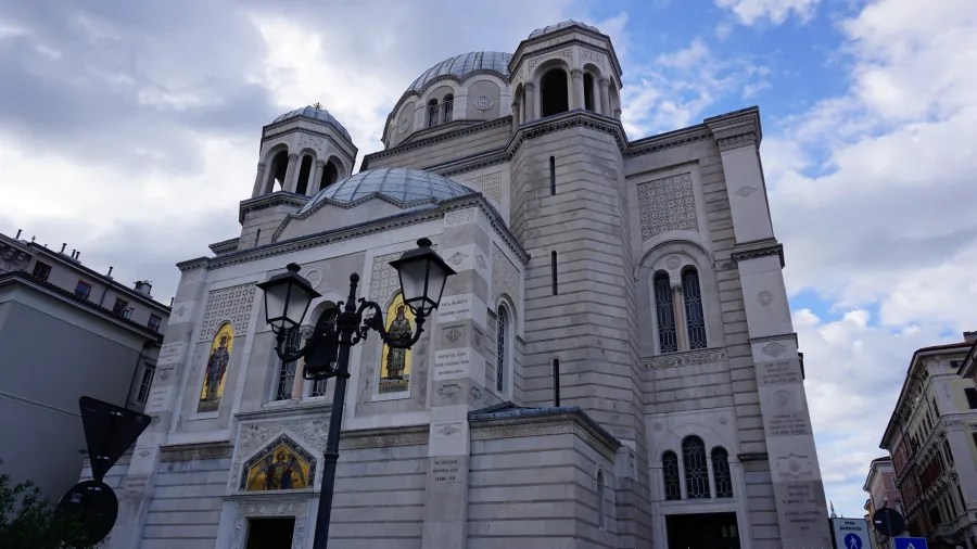 Ansicht einer beeindruckenden Kirche mit Kuppeln und dekorativem Mauerwerk, unter einem bewölkten Himmel.