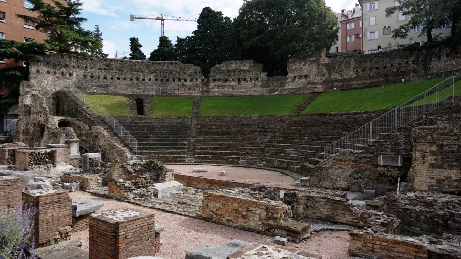 Ruinen eines antiken Theaters mit sichtbaren Steinstufen und Grashügeln im Hintergrund.