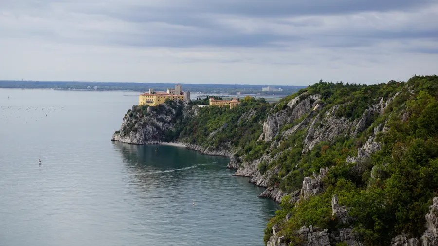 Aussicht auf eine Küstenlandschaft mit einem historischen Gebäude auf einer Klippe, umgeben von Bäumen und Wasser.