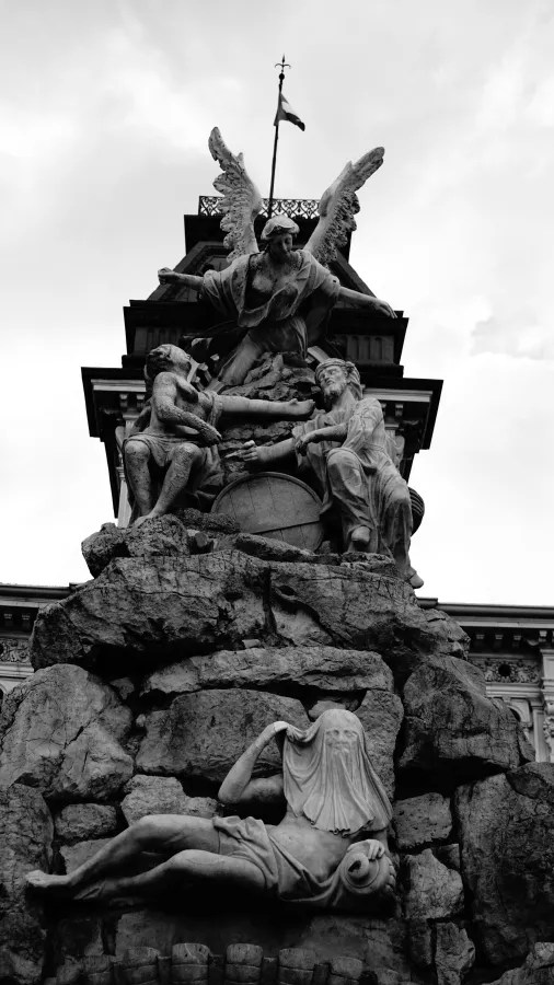 Skulpturen eines Denkmals mit einer Engelstatue an der Spitze, umgeben von weiteren Figuren auf einer steinernen Basis, im Schwarz-Weiß-Stil.