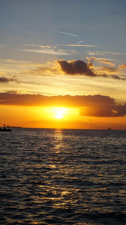 Sonnenuntergang über dem Wasser mit reflektierenden Wellen und bewölktem Himmel.