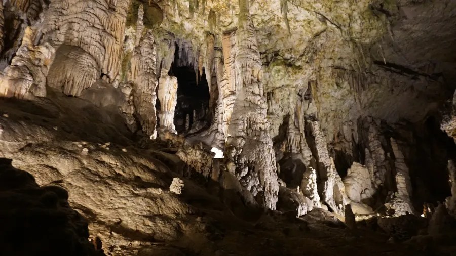 Eine dunkle Höhle mit beeindruckenden Stalaktiten und Stalagmiten, die von sanftem Licht beleuchtet wird.