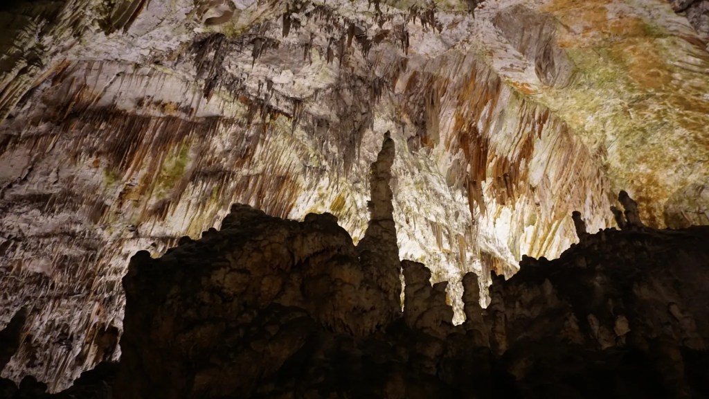Innenansicht einer Höhle mit beeindruckenden Stalaktiten und Stalagmiten, beleuchtet von warmem Licht.