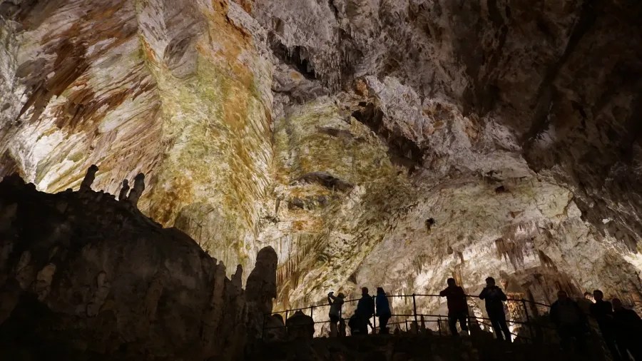 Eine beeindruckende Höhle mit leuchtenden Stalaktiten und Stalagmiten, während Besucher entlang eines Geländers stehen und die Umgebung erkunden.