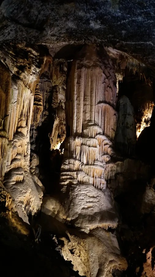 Eine beeindruckende Tropfsteinhöhle mit beleuchteten Stalagmiten und Stalaktiten in verschiedenen Formen und Texturen.