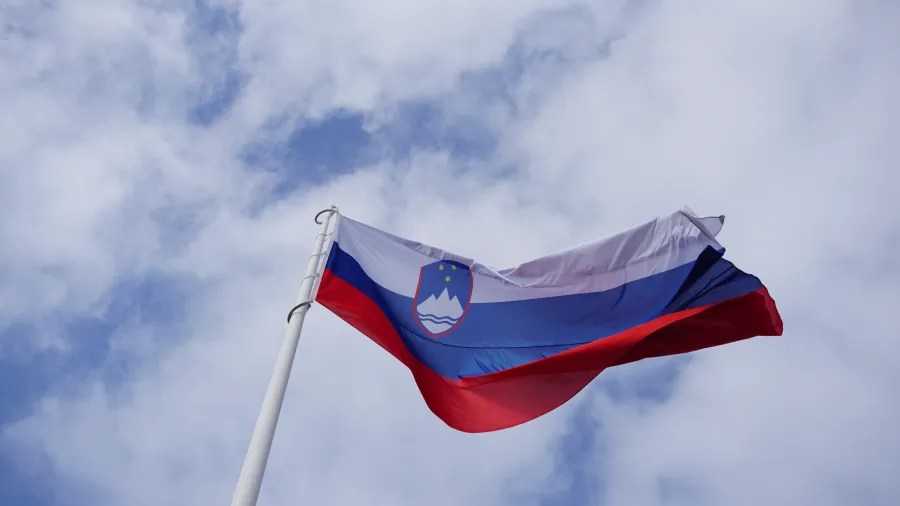 Flagge Sloweniens, die bei blauem Himmel mit Wolken weht.