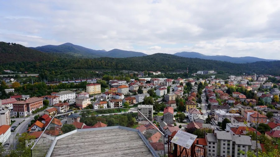 Panoramablick auf eine Stadt umgeben von Bergen und Hügeln mit einer Vielzahl von Wohnhäusern und roten Dächern.
