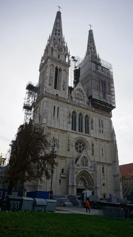 Die Kathedrale von Zagreb mit zwei Türmen, teilweise eingerüstet und renoviert, vor überwiegend bewölktem Himmel.