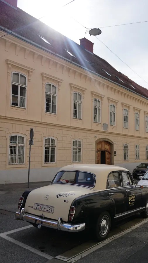 Ein klassisches Auto geparkt vor einem historisches Gebäude mit mehreren Fenstern.