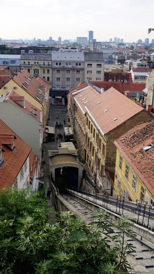 Blick über die Dächer einer Stadt mit einer Steinstraße, die zu einer Standseilbahn führt, umgeben von historischen Gebäuden.