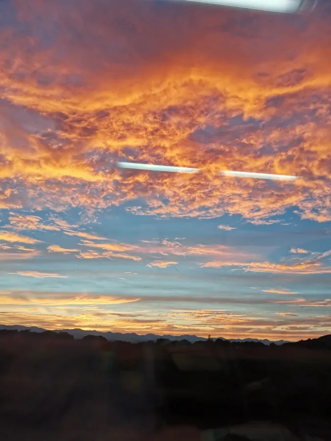 Blick auf einen bunten Sonnenuntergang mit orangefarbenen und blauen Wolken am Himmel über Bergen.