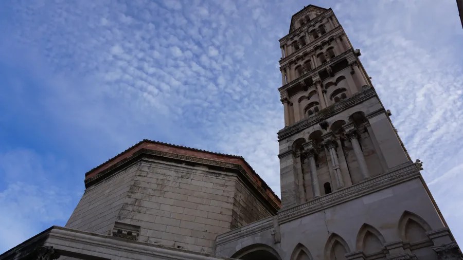 Low-angle view of the stone bell tower of Saint Domnius Cathedral against a wispy sky.