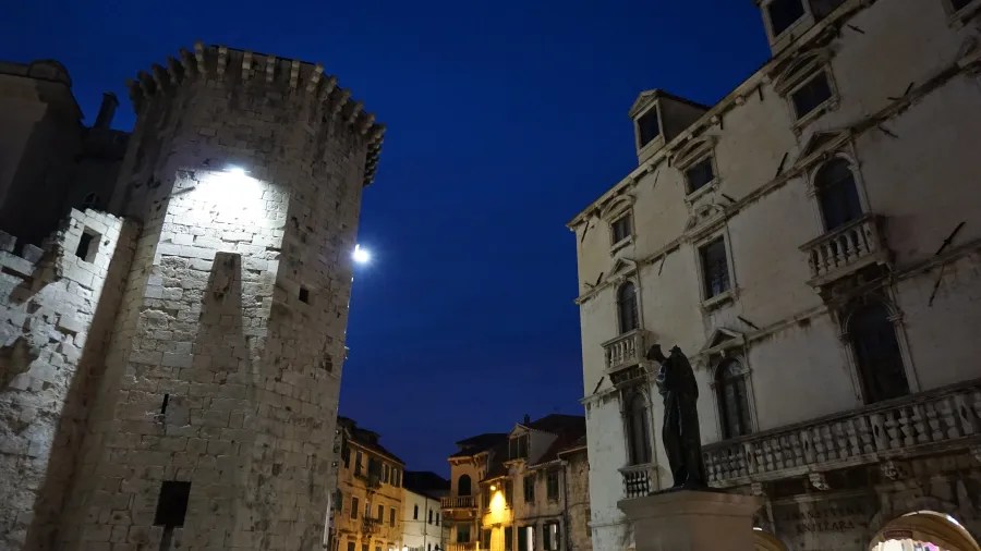 Stone Venetian tower and historic buildings in a city square under a twilight sky.