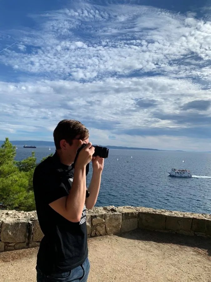 A person taking a photo of a coastal landscape with boats on the sea