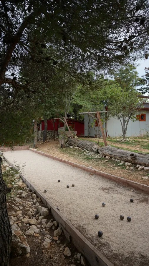 A rustic outdoor bocce court with metal balls scattered on its sandy surface
