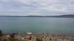 Calm turquoise lake with a rocky shore, a small red chair, and distant rolling hills.