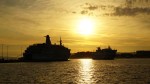 Two Jadrolinija ferries in a harbor with a bright golden sunset reflecting on the water.