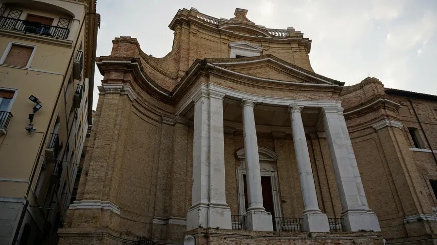 Classical brick building with a curved facade and white columned portico in an urban setting