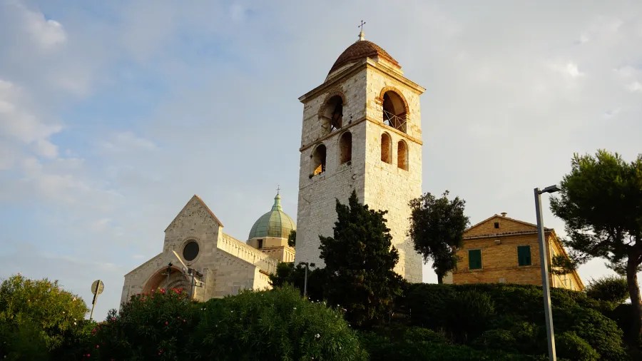 Historic stone cathedral with a tall bell tower and a green dome on a hill.