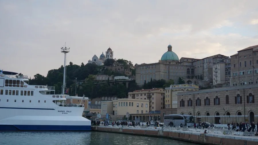 Large white ferry MARKO POLO RIJEKA docked at a harbor with historic hillside buildings