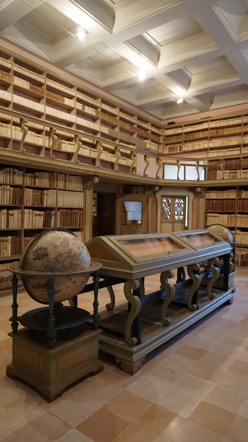Historic library interior featuring floor-to-ceiling bookshelves, a large globe, and glass display cases.