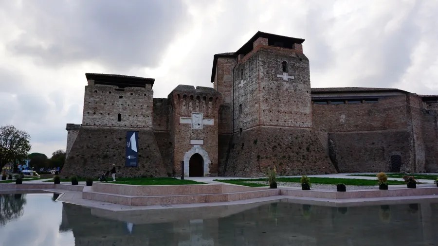 The brick walls and towers of Castel Sismondo fortress reflected in a foreground pool