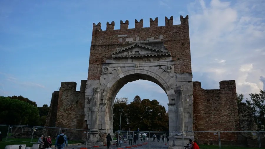 Ancient Roman stone and brick archway with a medieval crenellated top against a blue sky