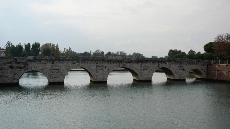 Ancient five-arched stone bridge crossing a calm river under an overcast sky.
