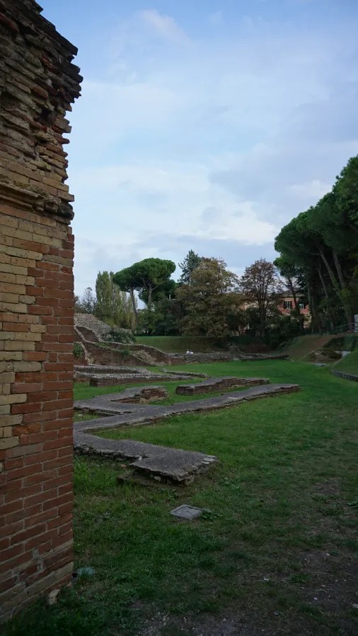 Ancient brick ruins and stone foundations within a grassy field and surrounding trees.