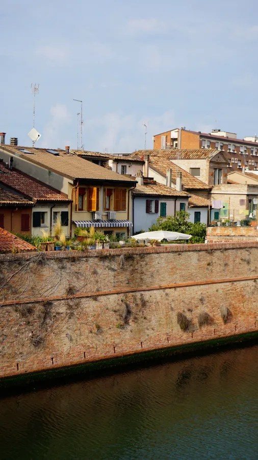Tiled roof houses behind an old brick wall along a canal.