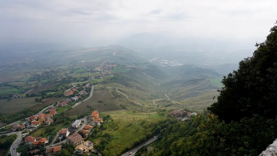 Hazy aerial view of hillside villages and winding roads in a rolling green landscape