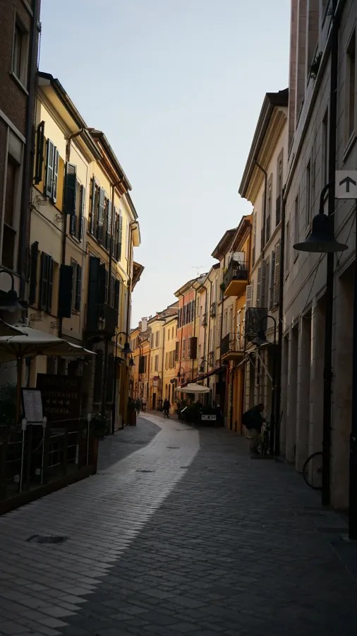 Narrow cobblestone street lined with historic buildings and outdoor cafe seating.