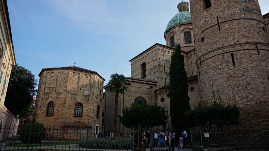 Historic brick architecture featuring an octagonal baptistery, domed cathedral, and cylindrical bell tower.