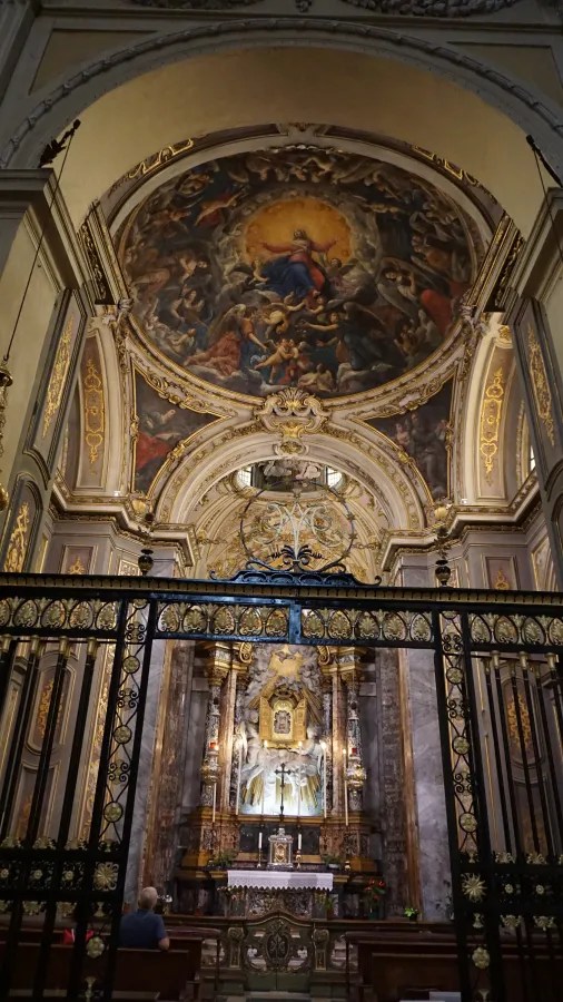 Ornate church chapel interior featuring a large domed ceiling fresco above a golden altar.