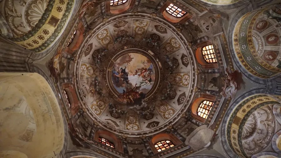 Ornate church dome ceiling featuring intricate frescoes, religious symbols, and small arched windows