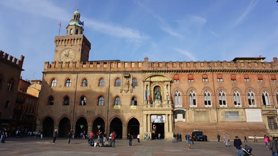 Large historic brick building with a clock tower and arched porticos in a city plaza