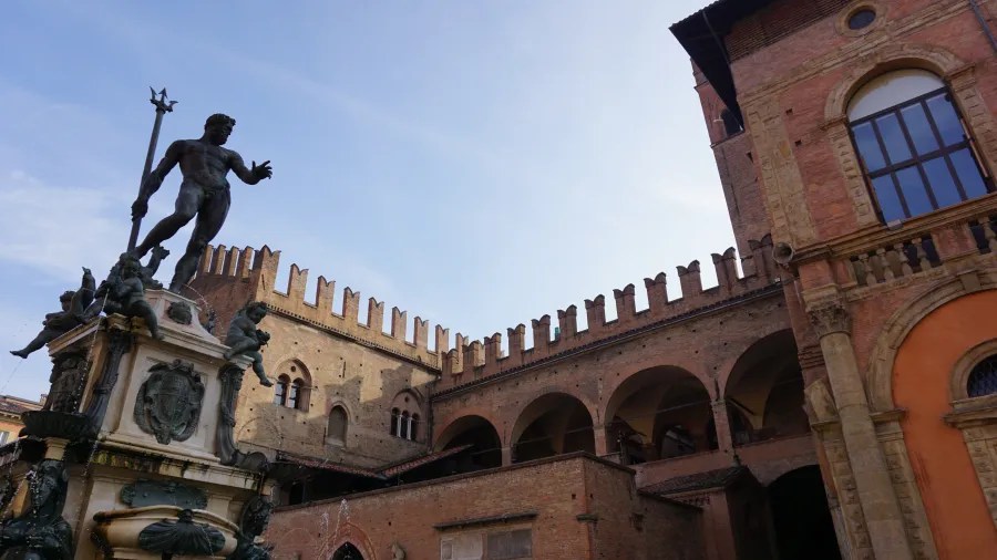 Bronze statue of Neptune on a fountain before historic brick buildings in Bologna