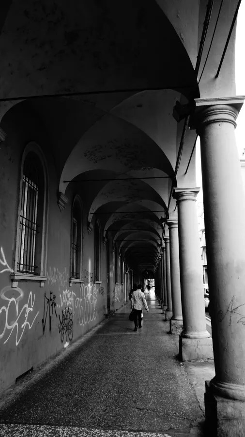 Black and white perspective of a long, vaulted portico with stone columns and graffiti.
