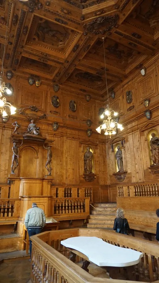 Ornate wooden anatomical theater with tiered seating, carved ceiling, and statues in wall niches.