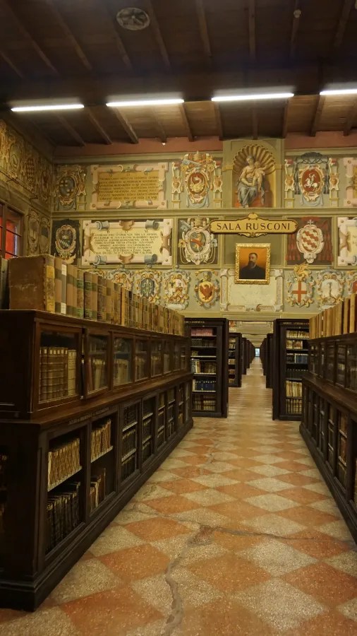 Sala Rusconi library hallway with dark wood bookshelves and walls decorated with coats of arms.