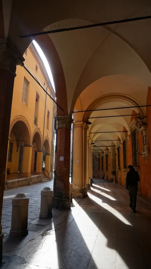 Sunlight casting long shadows through a series of historic arched porticoes over a sidewalk.