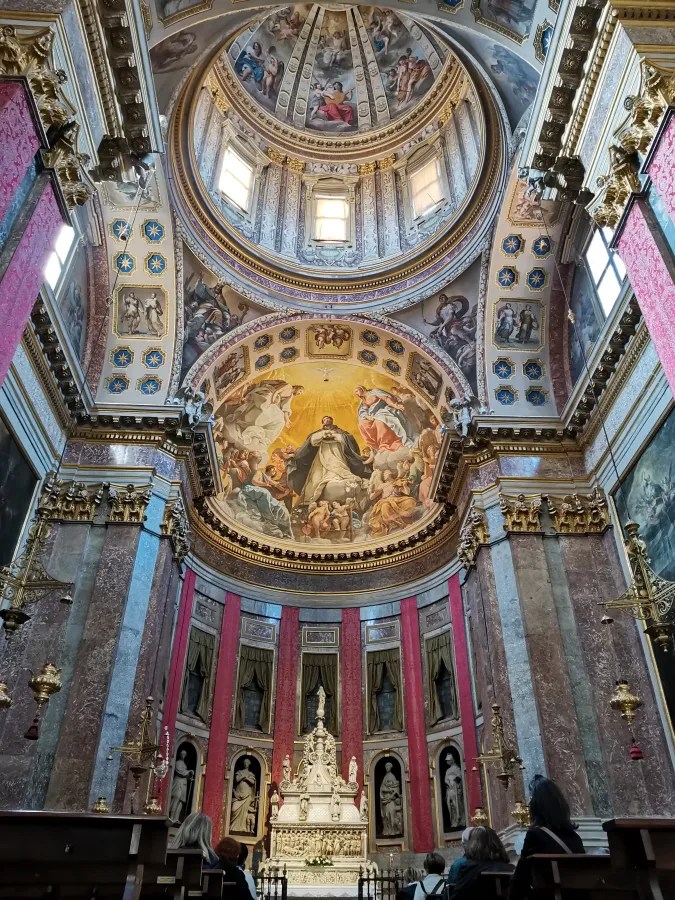 The ornate interior of a cathedral featuring a frescoed dome and highly decorated altar