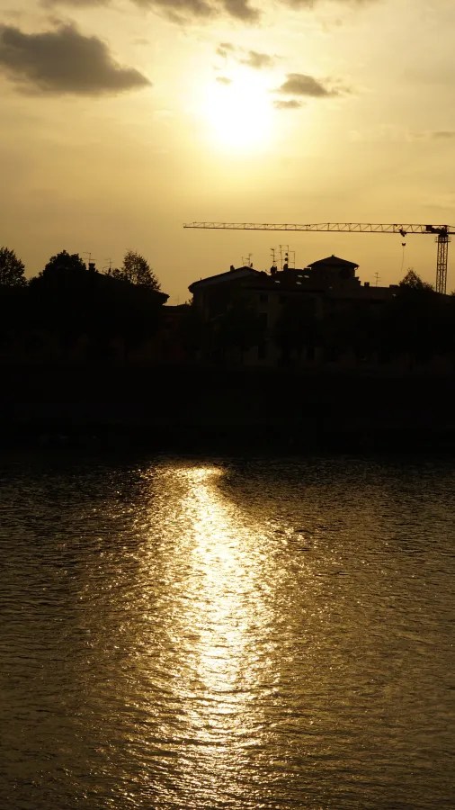 Golden sunset reflecting on water with a silhouetted city skyline and construction crane.